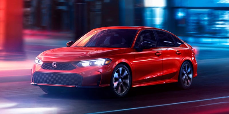 A shiny red Honda Civic sedan driving quickly at night with blurred blue and red streaked lights in the background.