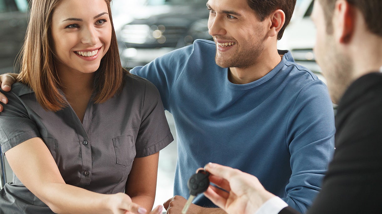 A smiling couple receives car keys from a salesperson.